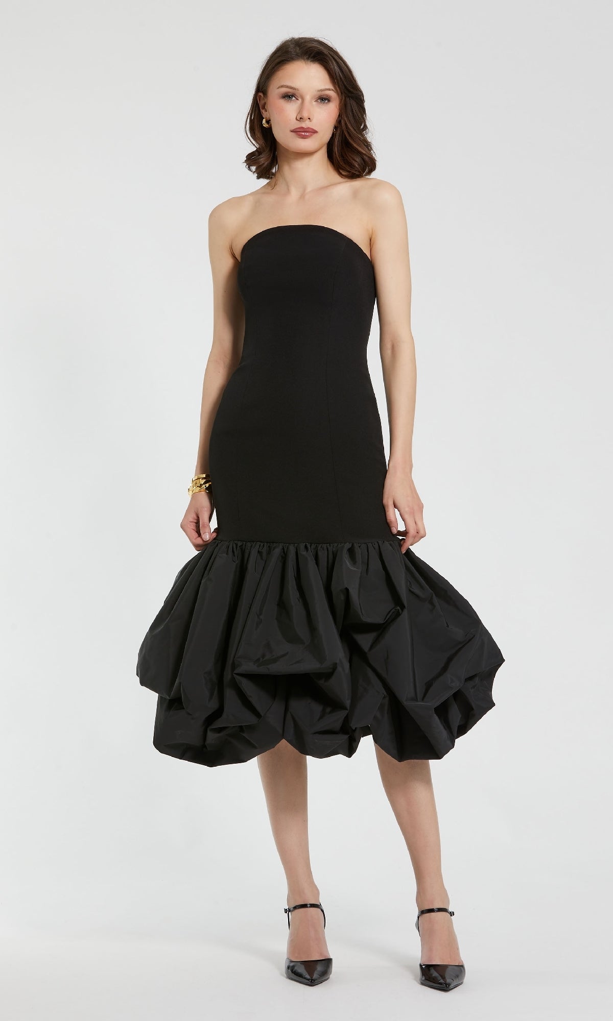 A woman wearing the Mac Duggal 21061 Black Midi Bubble Party Dress with a fitted bodice and voluminous bubble hem skirt, paired with black heels, stands against a plain white background.